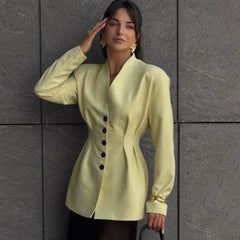 Woman wearing a light green blazer with black buttons against a gray tiled wall.