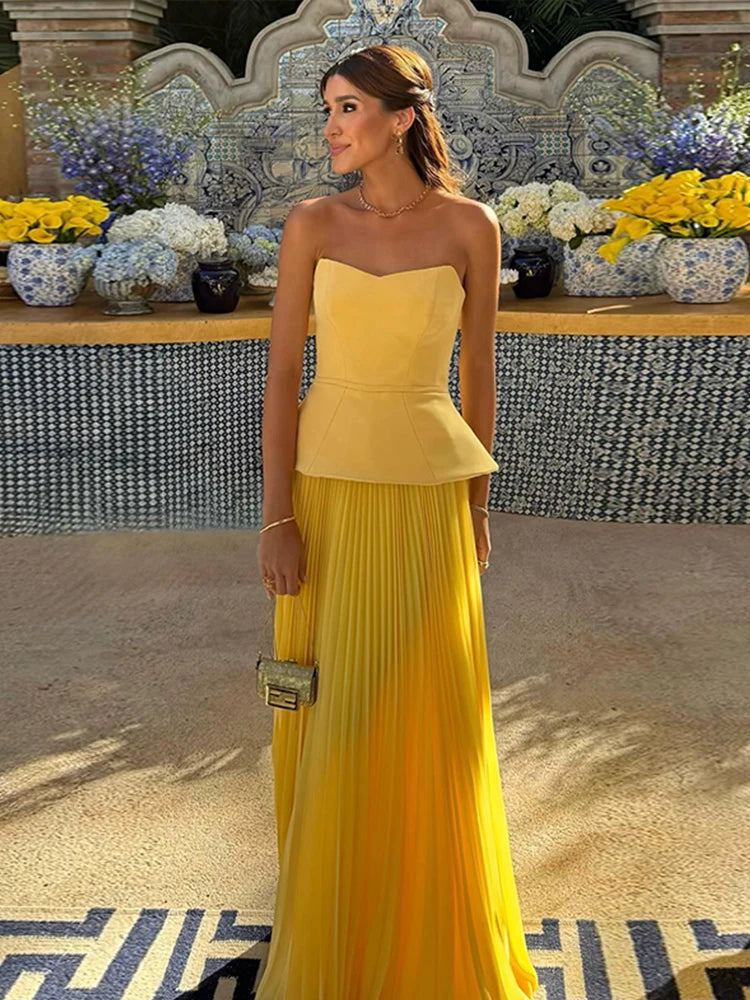Woman in a yellow strapless dress standing in front of a decorative wall with flowers.