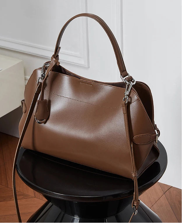 Brown leather handbag on a black pedestal against a white paneled wall.