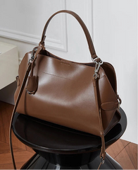 Brown leather handbag on a black pedestal against a white paneled wall.