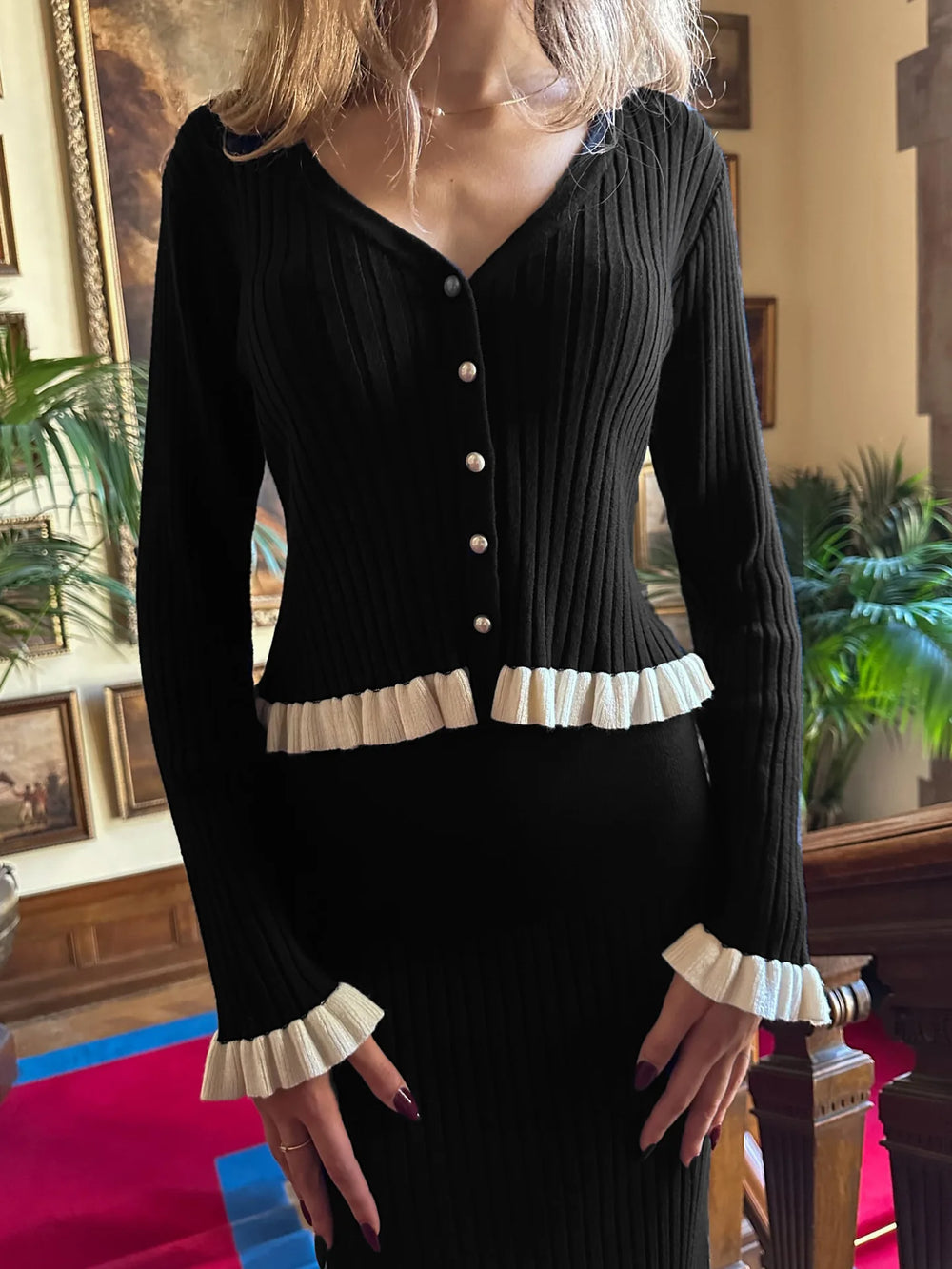 Person wearing a black cardigan with white trim in an indoor setting