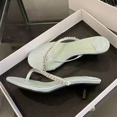 Pair of light green high-heeled sandals with rhinestone details on a reflective surface.