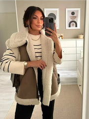 Woman taking a mirror selfie wearing a brown coat with white fur trim in a room.