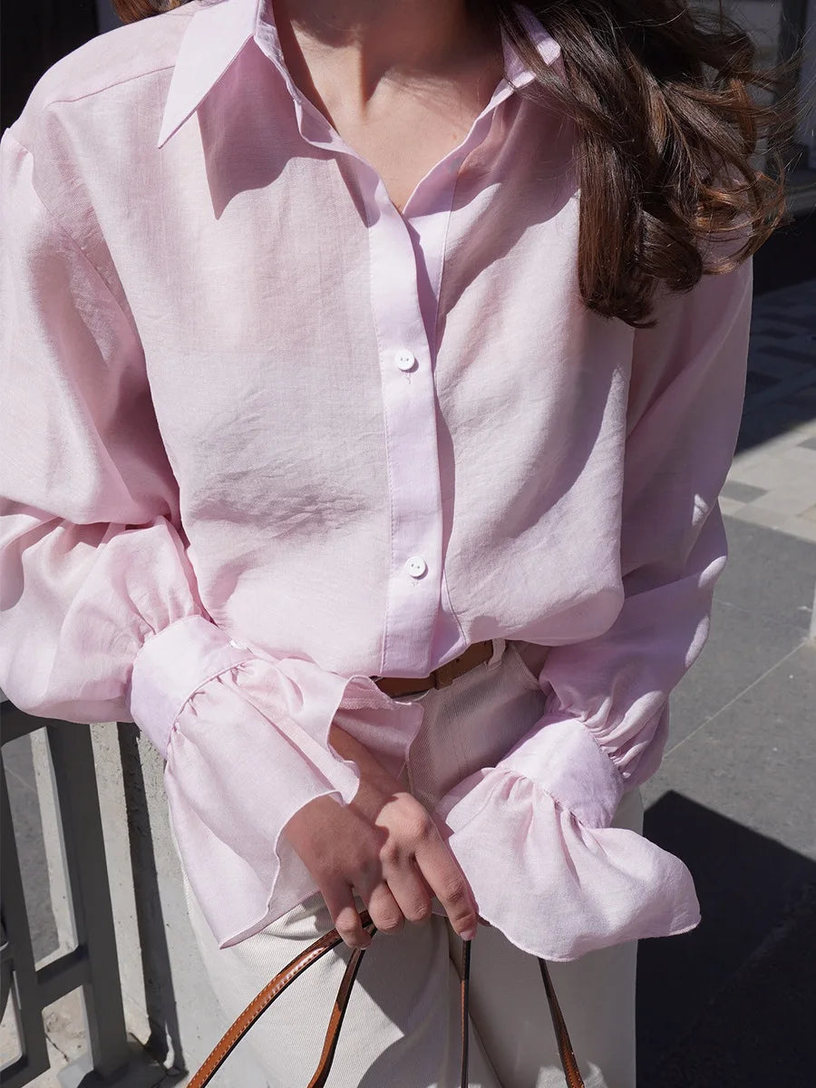 Person wearing a light pink shirt with ruffled sleeves outdoors.