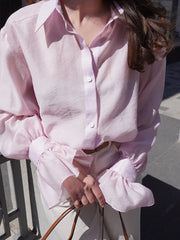 Person wearing a light pink shirt with ruffled sleeves outdoors.