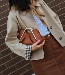 Person holding a brown handbag against a brick wall