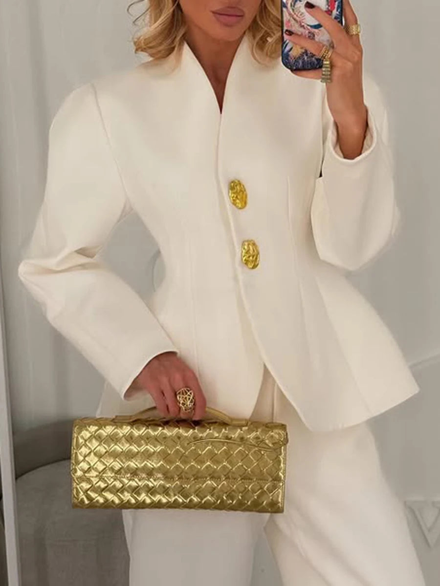 Person wearing a white suit with gold buttons holding a gold clutch.