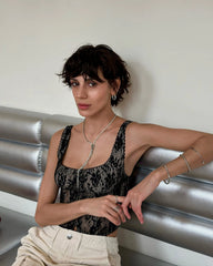 Woman posing on a metallic surface wearing a black lace top and beige pants.