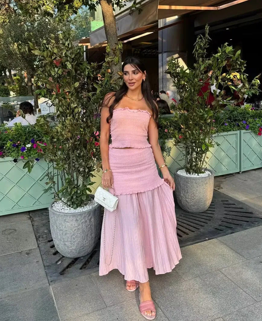 Woman in a pink dress standing outdoors with plants and a building in the background