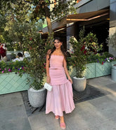 Woman in a pink dress standing outdoors with plants and a building in the background