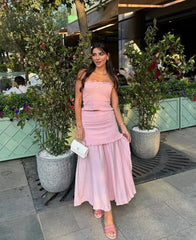 Woman in a pink dress standing outdoors with plants and a building in the background