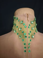 Mannequin wearing a beige garment with green gemstones on a black background