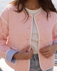 Person wearing a pink quilted jacket with white trim, gold buttons, and a white shirt underneath.