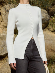 Person wearing a white ribbed long-sleeve shirt with a button-up front, standing outdoors with rocks and grass in the background.