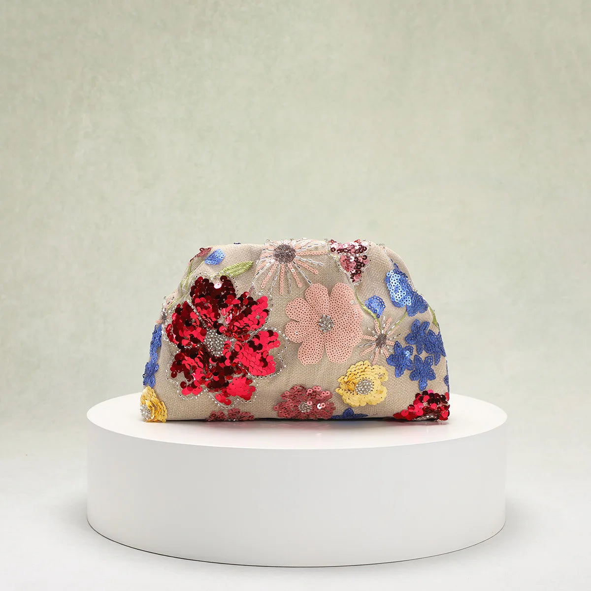 Floral embroidered clutch bag on a white pedestal against a light gray background