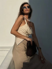 Woman in a beige dress holding a brown bag against a light background