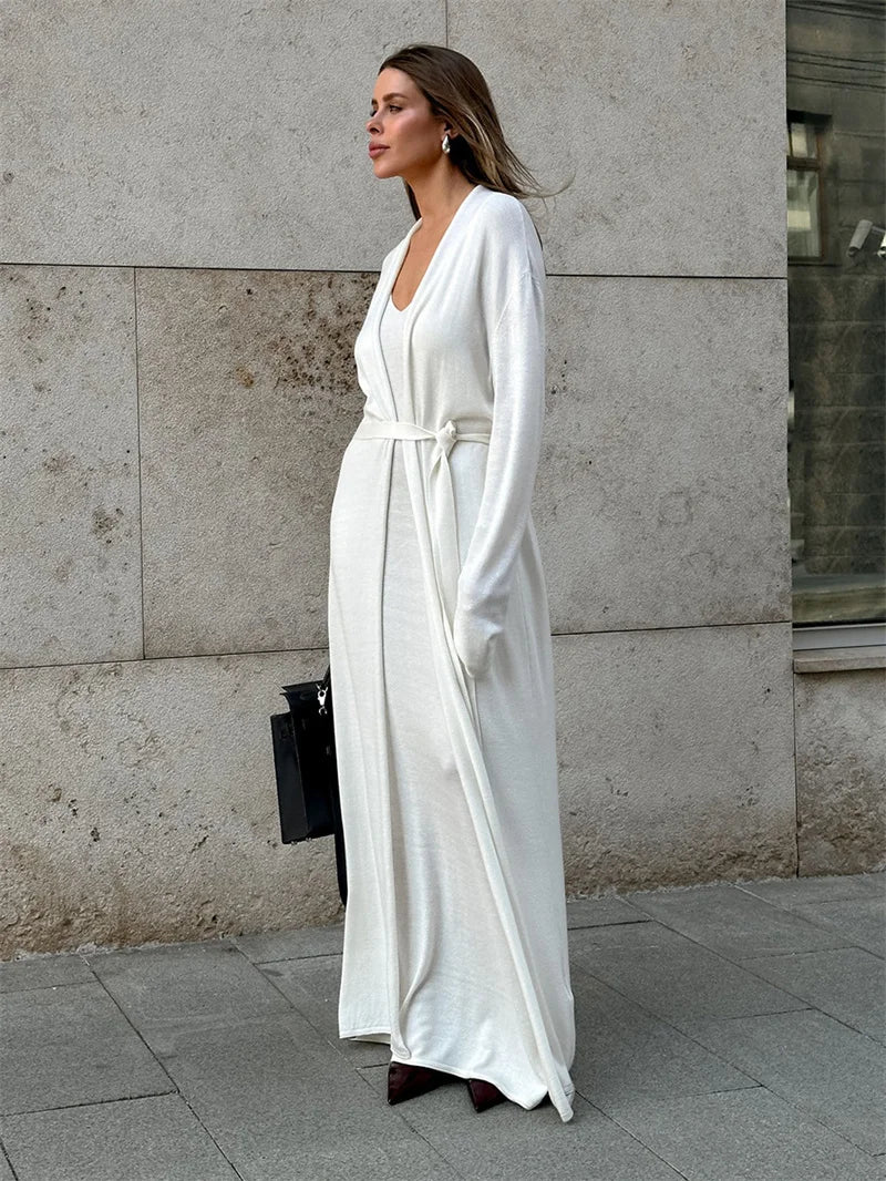 Woman in a white dress standing against a stone wall.