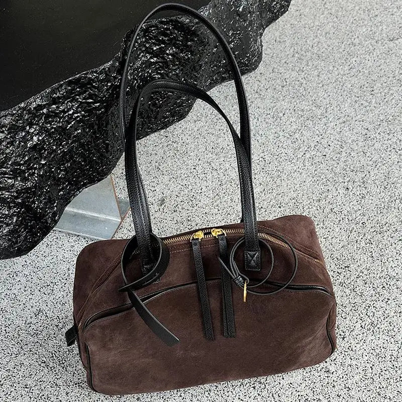 Brown handbag with black straps on a textured surface