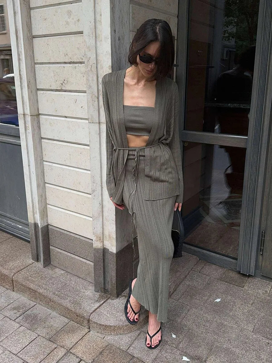 Woman in a gray outfit standing against a building wall.