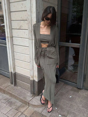 Woman in a gray outfit standing against a building wall.