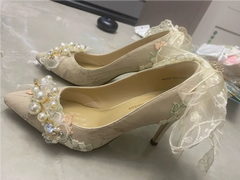 Beige high-heeled shoes with floral and pearl decorations on a light background