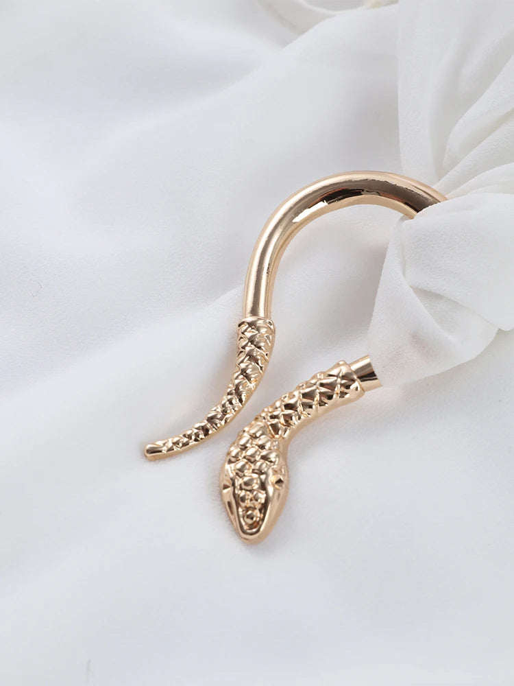 Gold snake-shaped earring on a white fabric background