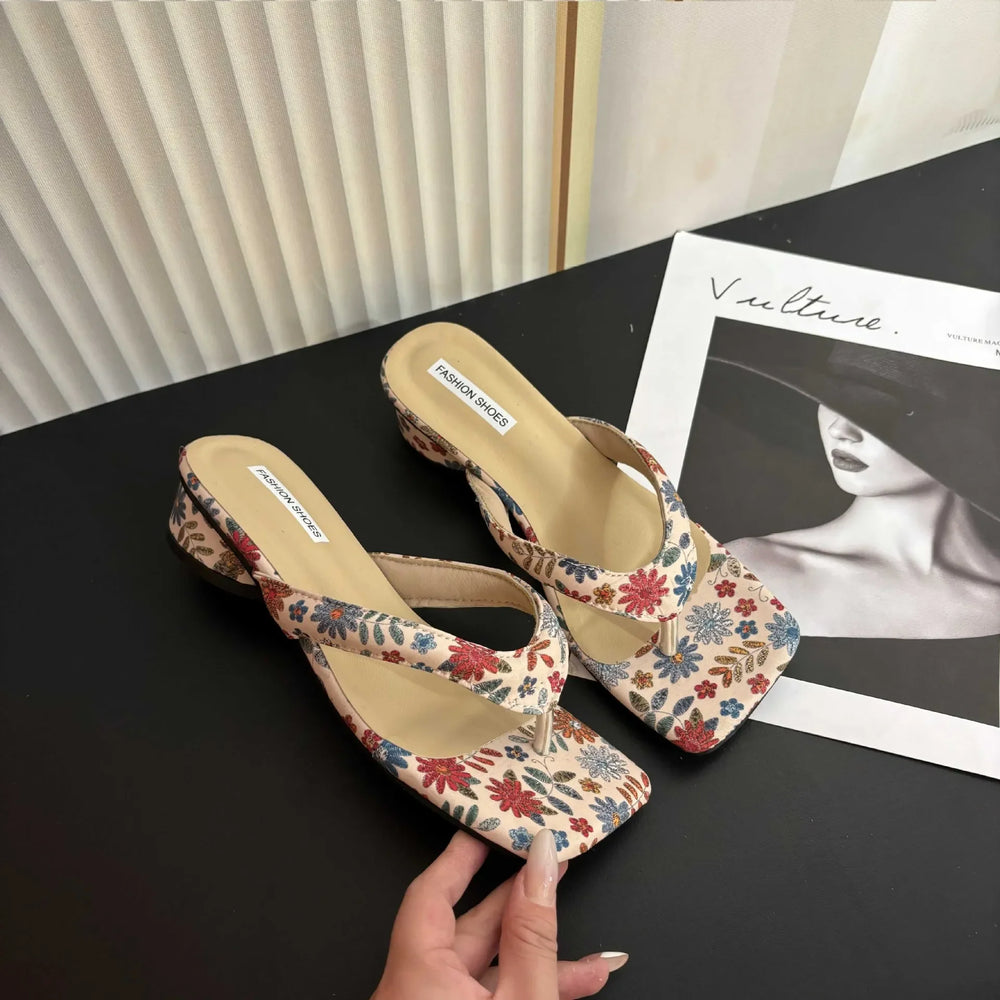 Pair of floral-patterned sandals on a black surface with a magazine in the background.
