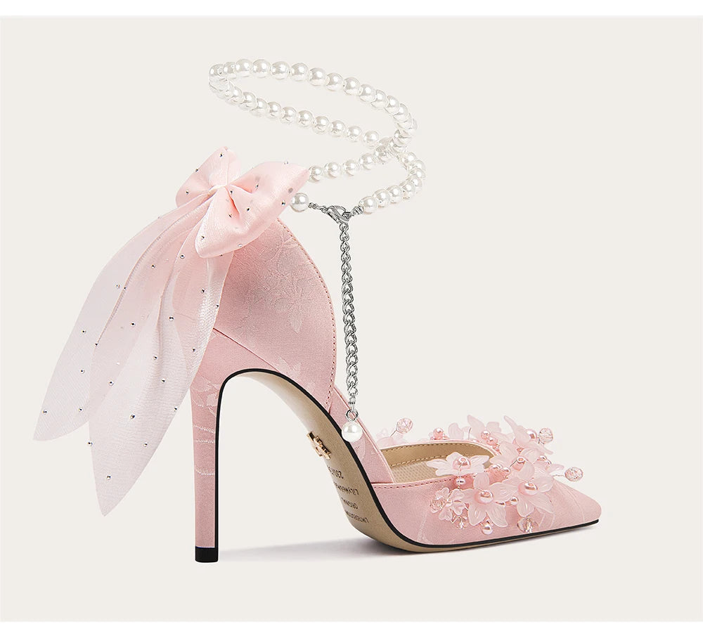 Pink high-heeled shoes with floral details and a matching handbag on a light gray background