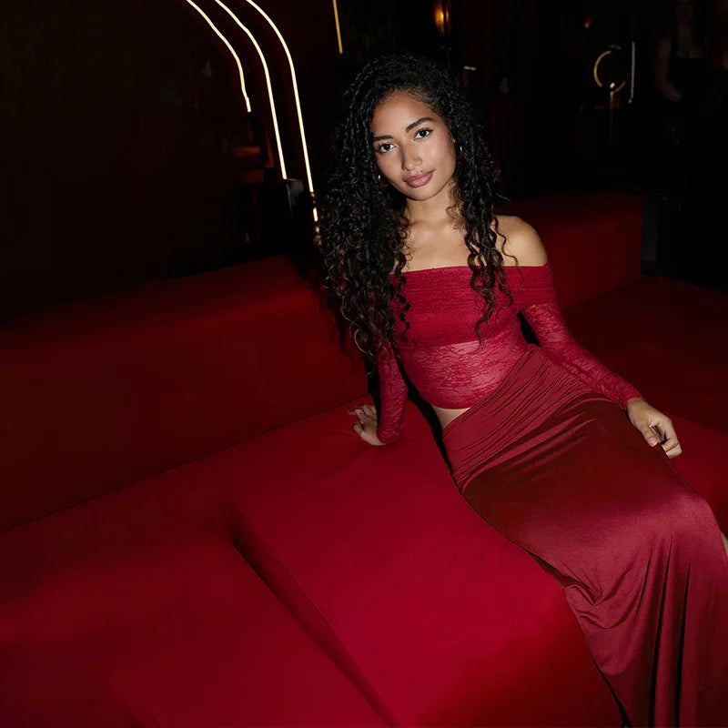 Woman in a red dress sitting on a red couch in a dimly lit room.