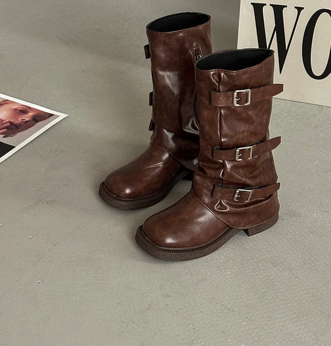 Pair of brown leather boots with buckles on a gray surface.