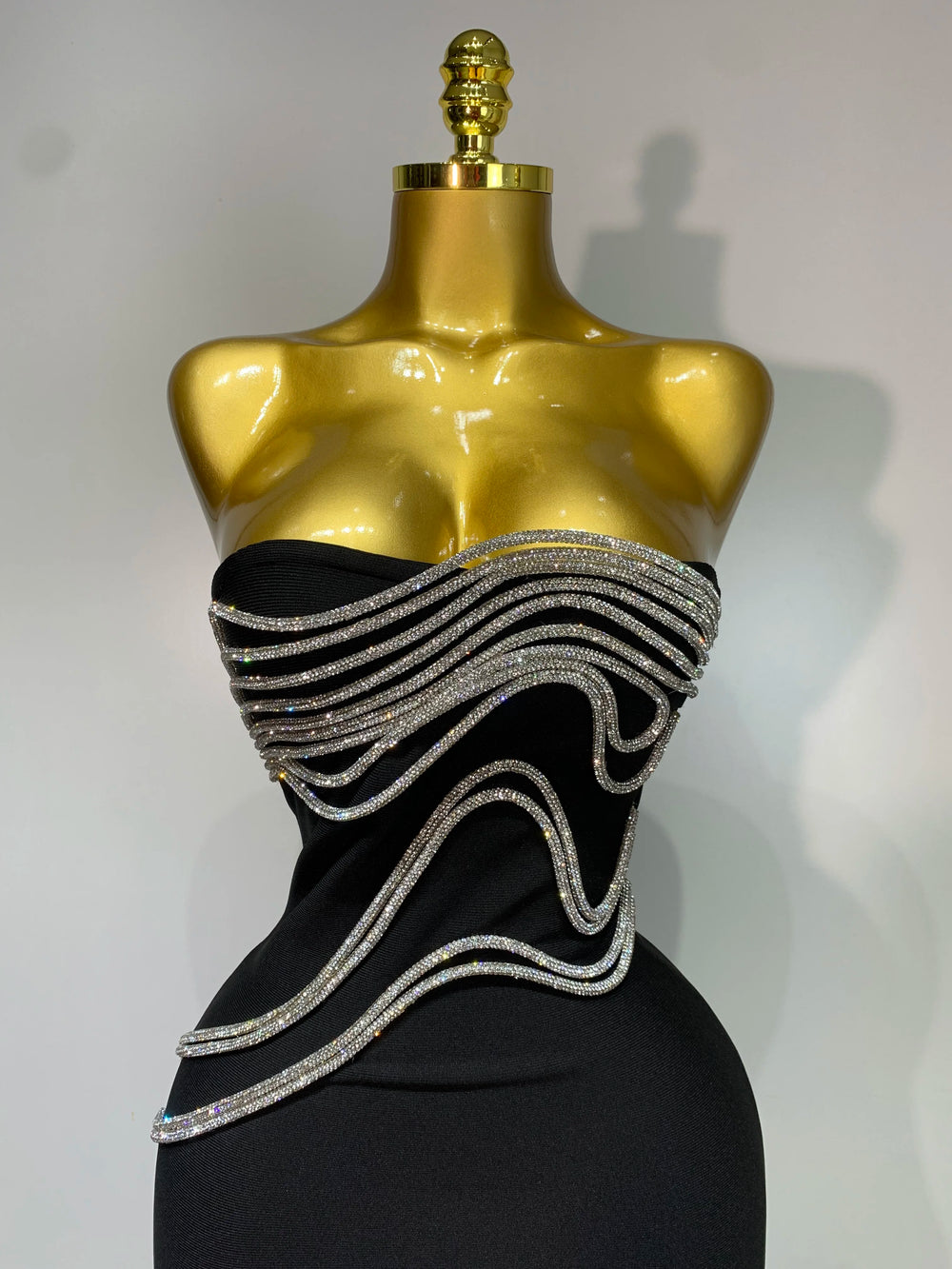 Black dress with silver embellishments on a gold mannequin against a white background