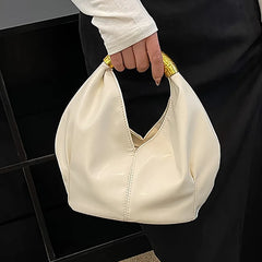 White soft PU leather dumpling shaped handbag with a textured gold metal handle, held by a hand.