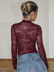 Person wearing a burgundy lace long-sleeve top and blue jeans against a neutral background