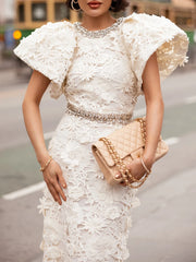 A person holding a beige quilted handbag with a gold chain strap, wearing a white lace gown.