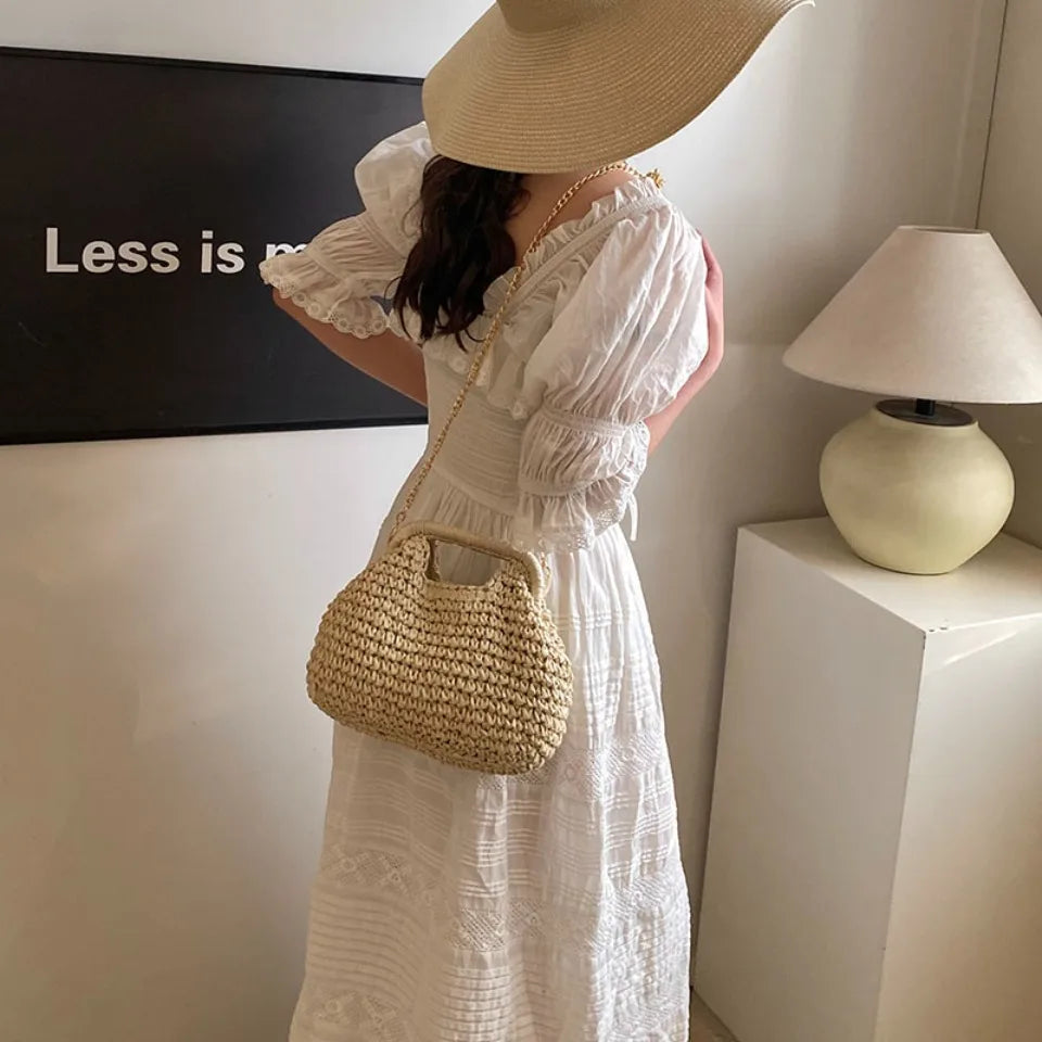 Woman in a white dress holding a straw bag indoors with a lamp and text on the wall.