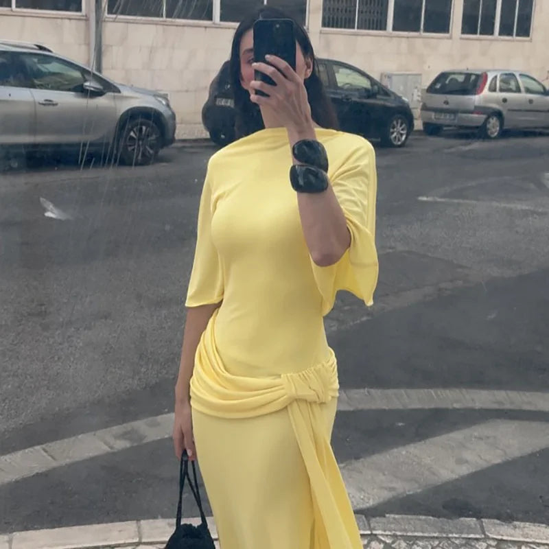 Person wearing a yellow dress taking a mirror selfie on a street with cars in the background.
