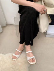 Person wearing black pants and white sandals sitting on a white rug.