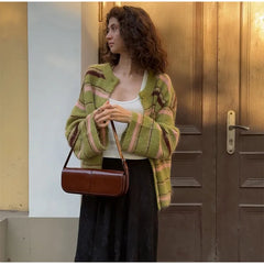Woman wearing a green and pink striped cardigan holding a brown handbag in front of a door.