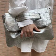 Person holding a silver crocodile-patterned clutch bag against a tiled wall background