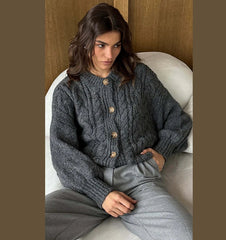 Person wearing a gray knitted cardigan sitting on a white couch.