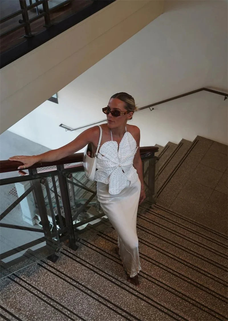 Woman in a white dress and sunglasses standing on a staircase.