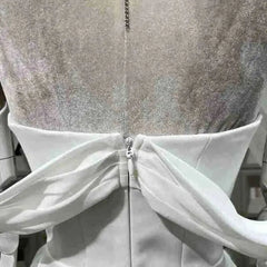 Close-up of a silver glittery dress with a white fabric overlay on a blurred background