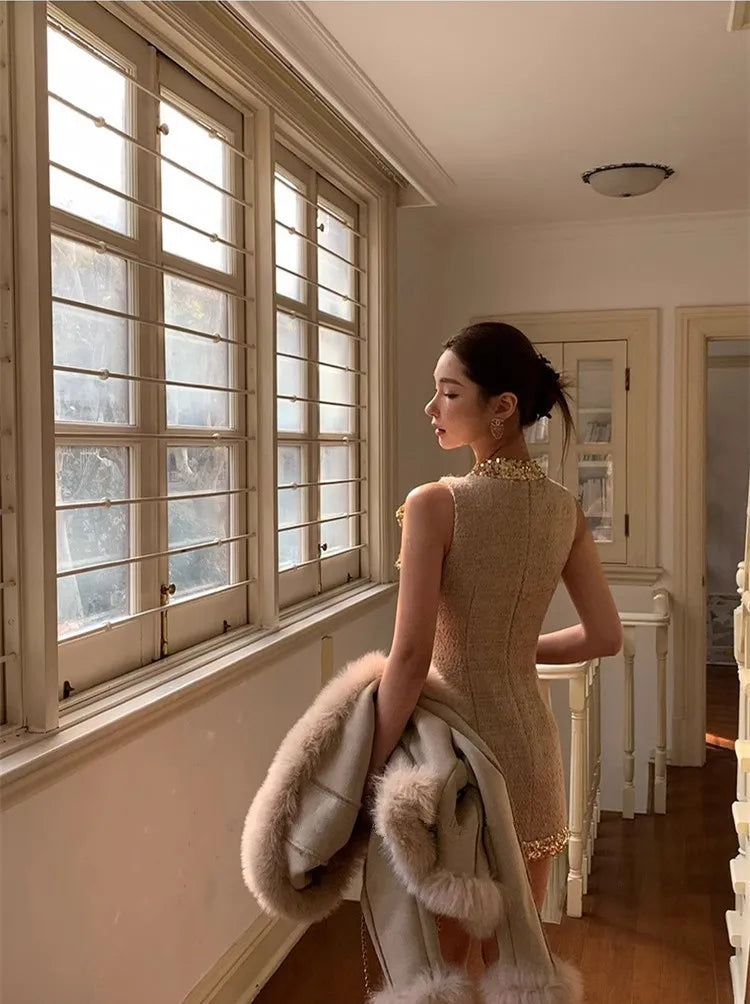 Woman in a beige dress standing by a window in a room with wooden floors.