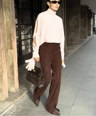 Woman in a light pink blouse and brown pants walking outdoors.