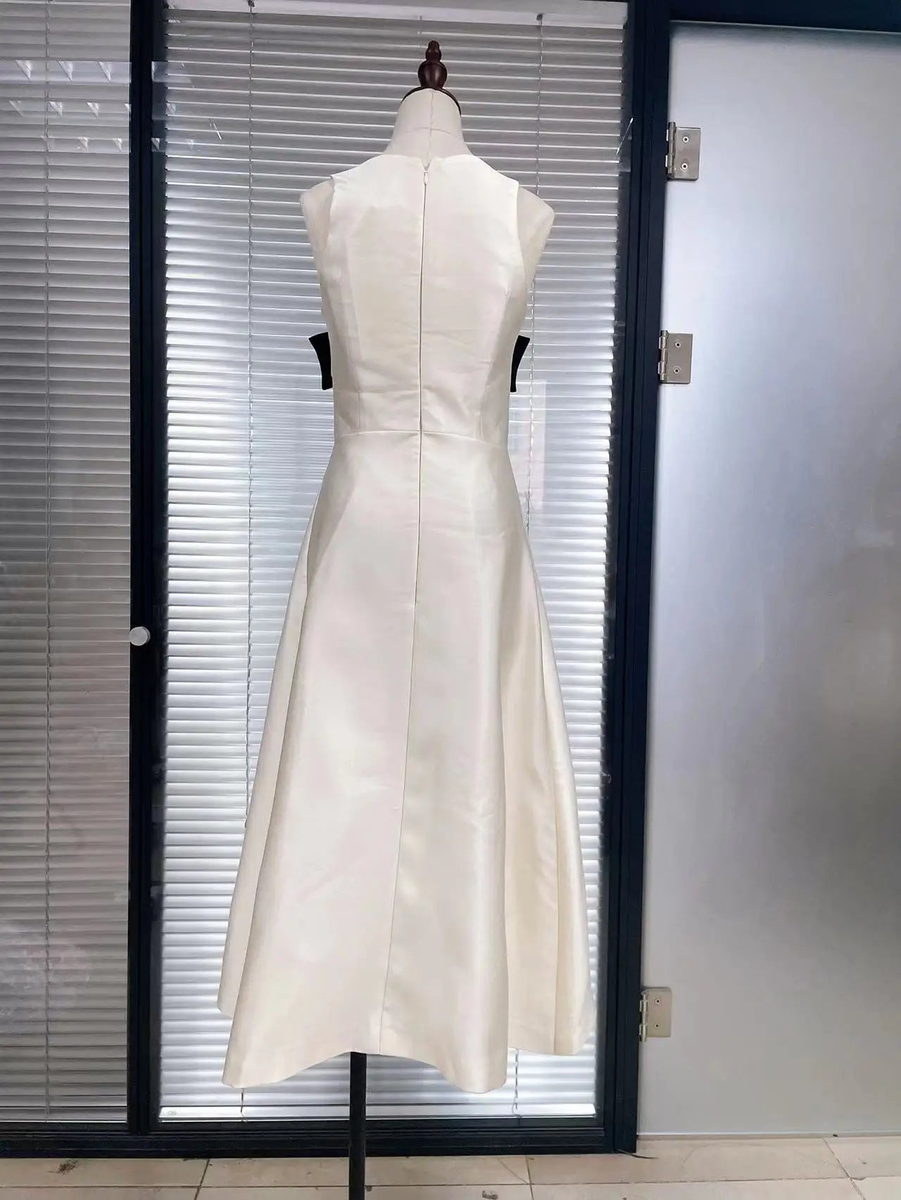 White dress on a mannequin against a glass door.