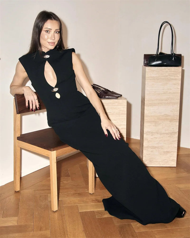 Woman in a black dress sitting on a chair with a black handbag beside her.
