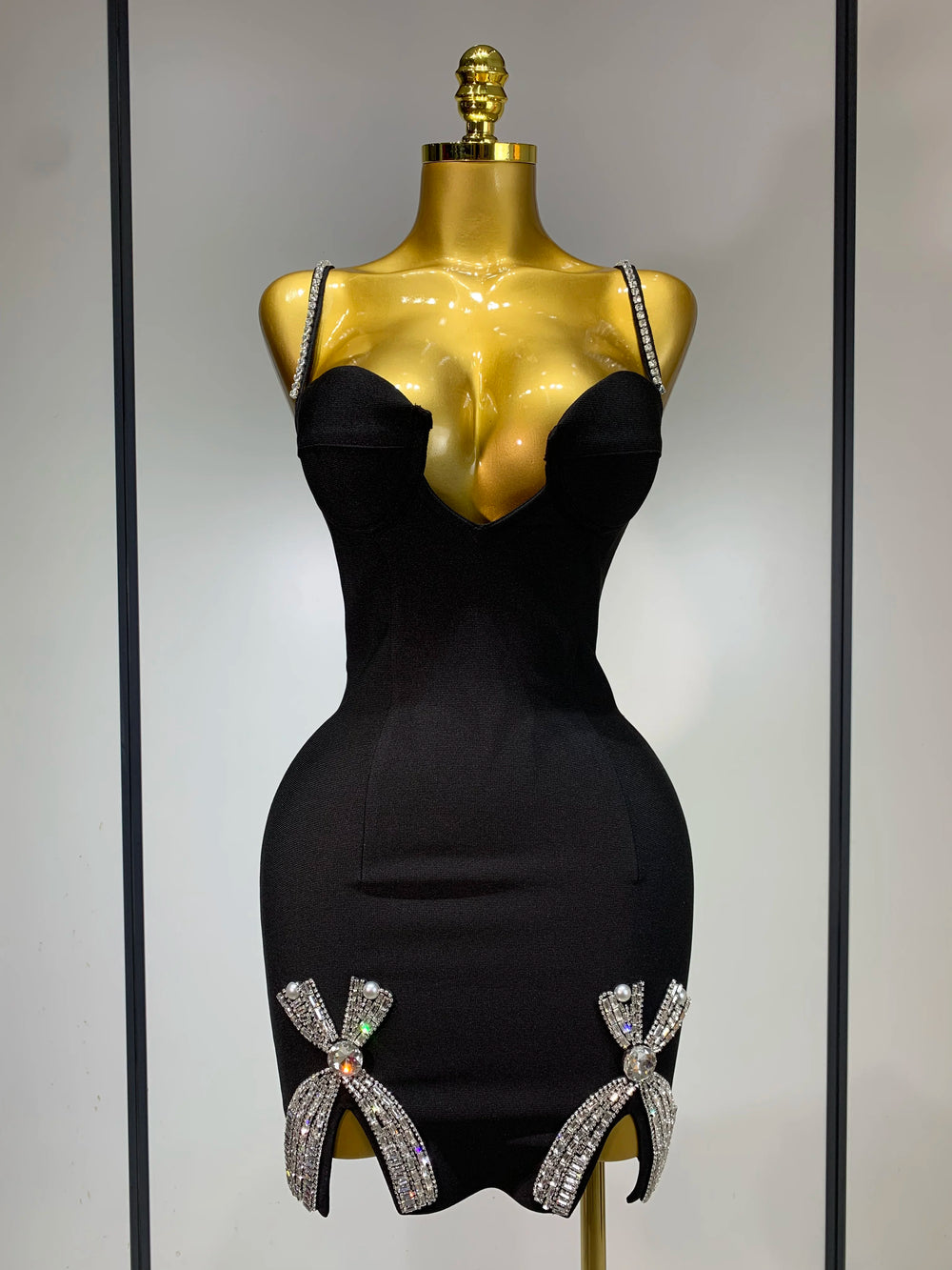 Black dress with decorative bows on a gold mannequin against a neutral background