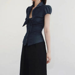 Woman wearing a dark blue blouse with puff sleeves and a black skirt on a light gray background