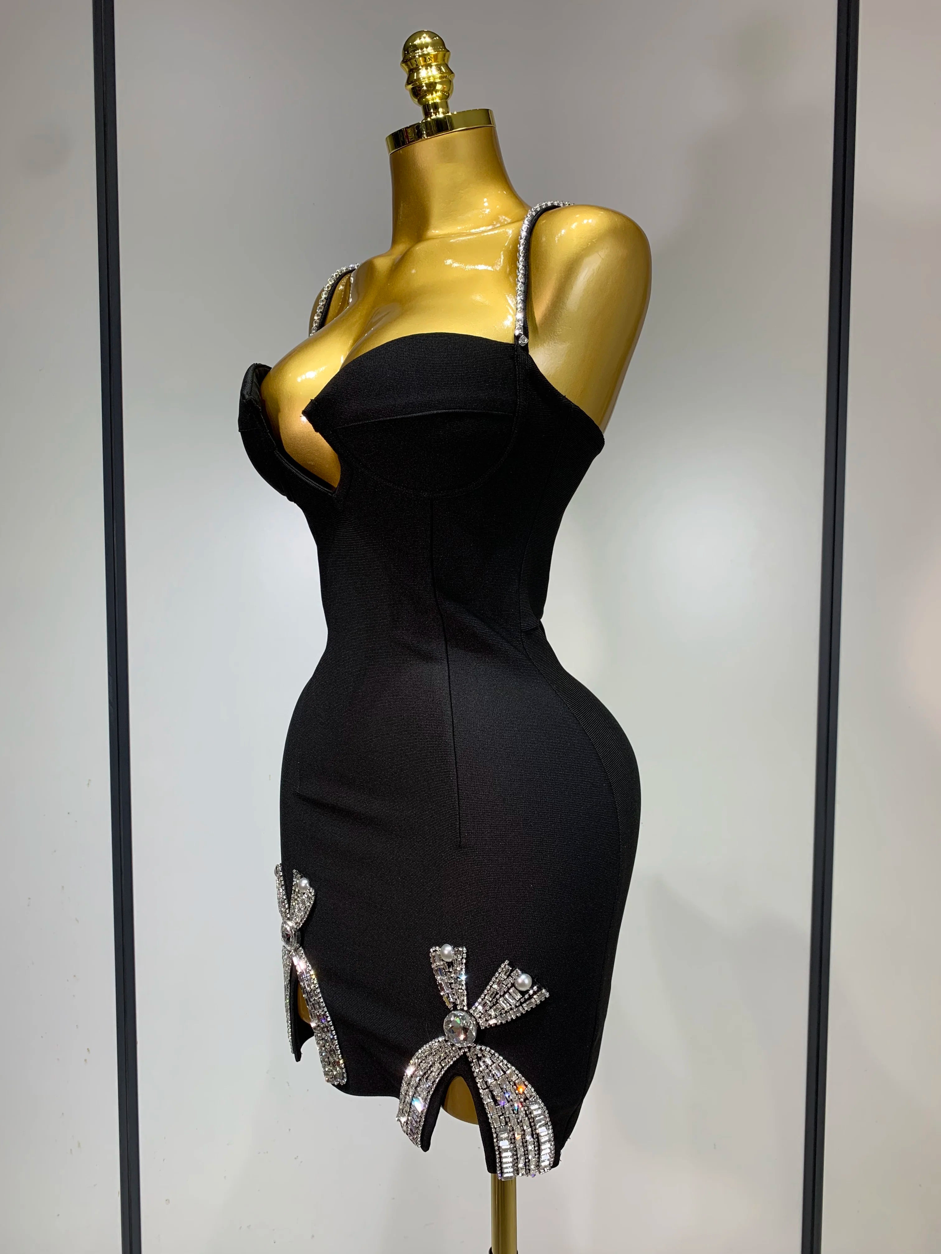 Black dress with decorative bows on a gold mannequin against a neutral background