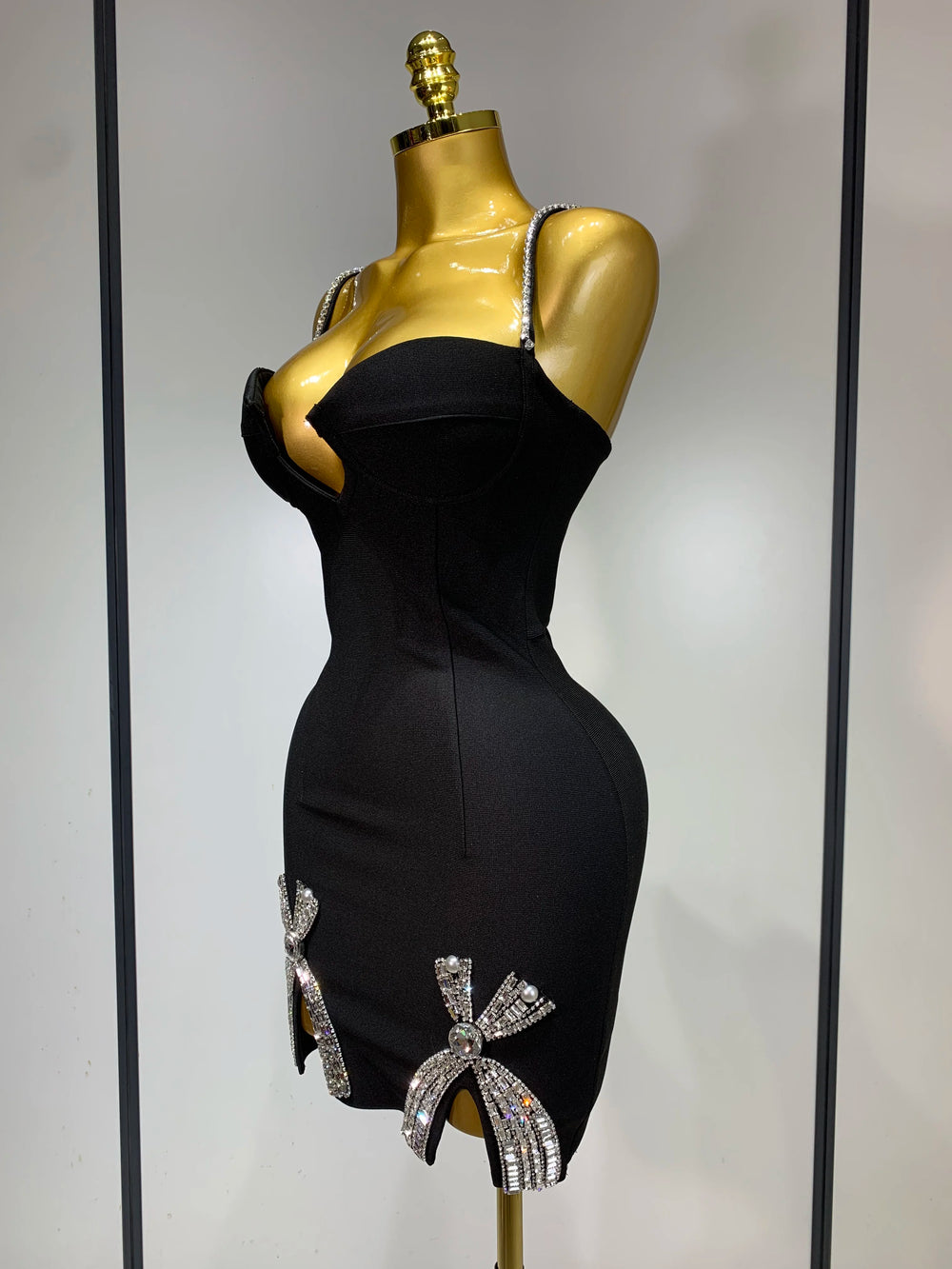 Black dress with decorative bows on a gold mannequin against a neutral background